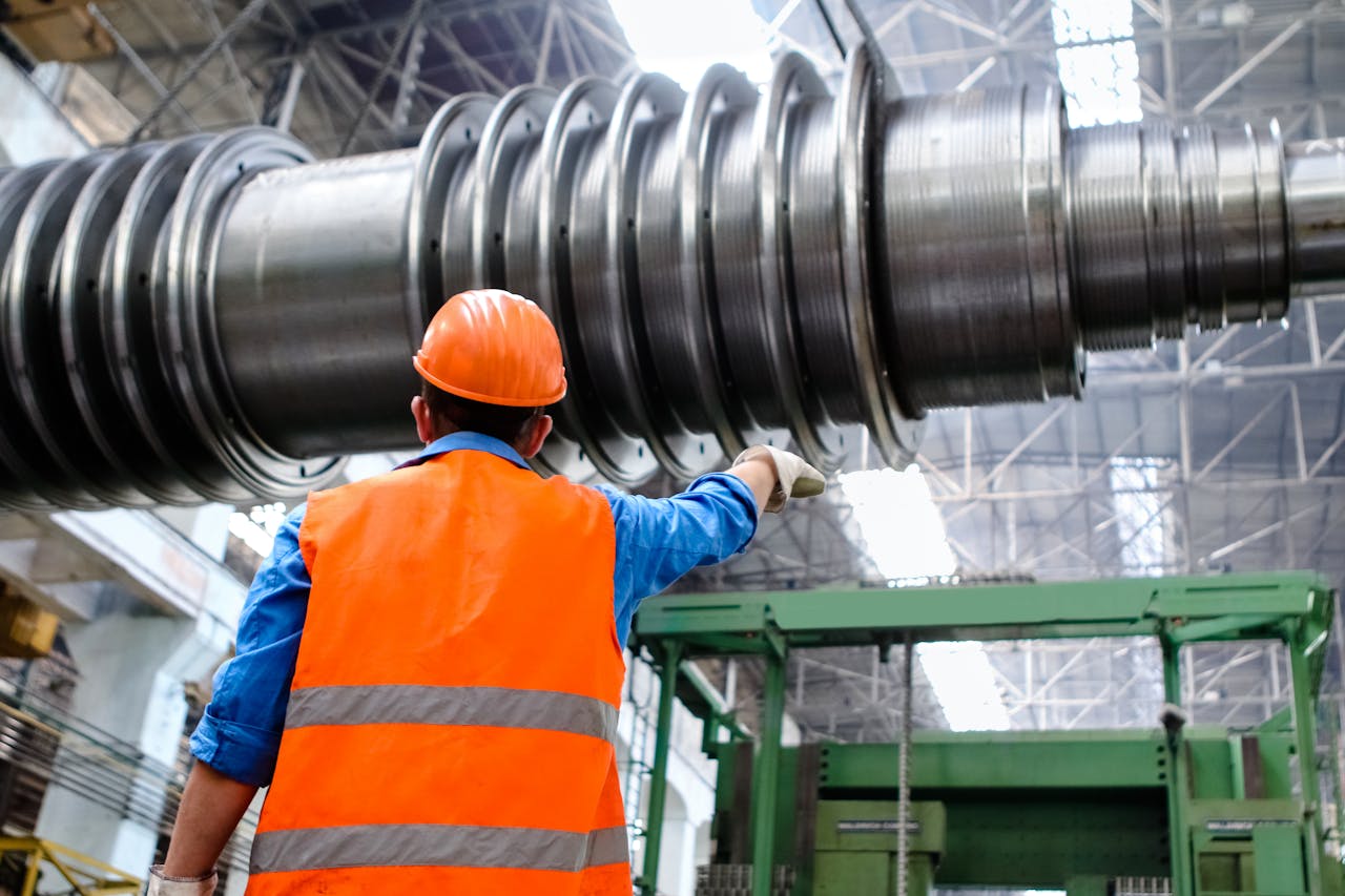 why-choose-us Engineer in high visibility vest and hard hat inspecting large machinery in factory setting.